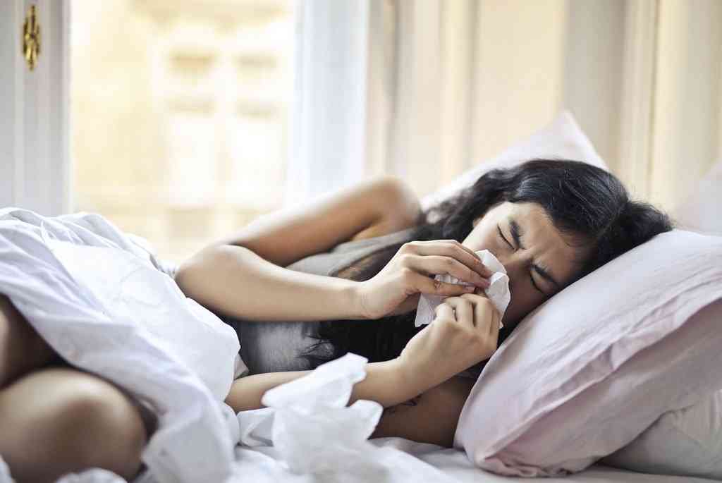 Женщина с простудой лежит в постели и сморкается