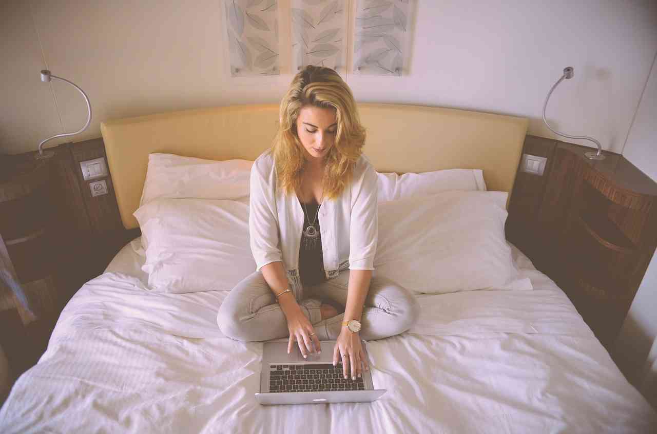 Женщина сидит на кровати и работает за компьютером